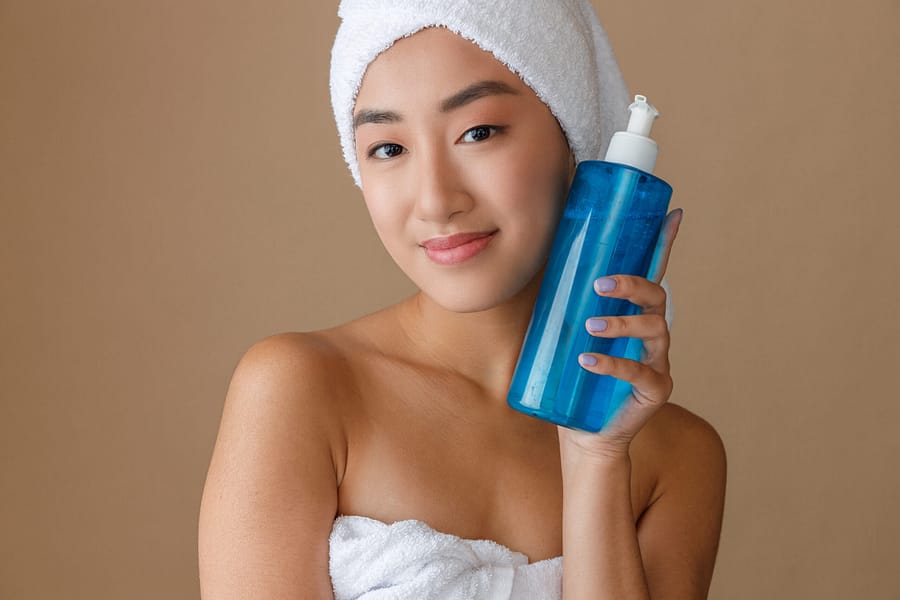 Smiling female person with moisturizing lotion in her hand standing in studio. Isolated on light brown background